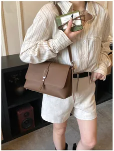 Détail d'un sac bandoulière en cuir marron texturé avec boucle argentée et petit portefeuille