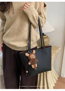 Detail of black pebbled leather tote bag featuring a cute brown teddy bear keychain charm