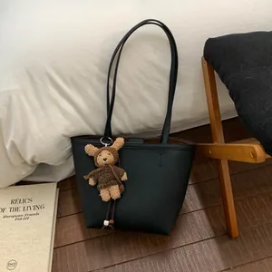 Detail of black textured leather tote bag with a cute brown teddy bear charm accessory