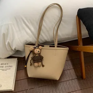 Detailed macro view of the beige lychee pattern tote bag with a cute teddy bear charm