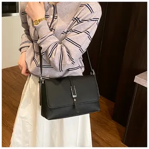 Gros plan sur la texture du cuir grainé noir et la boucle argentée du sac à bandoulière