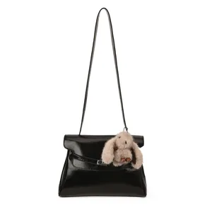 Chic black patent leather shoulder bag with a cute plush bunny charm on white background