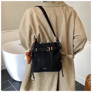 Detail der schwarzen matten Wildleder-Schultertasche mit goldener Schnalle und Bärenanhänger