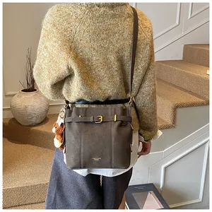 Schicke dunkelbraune Beuteltasche mit Lederriemen über einem gelben Strickpullover