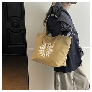 Detailed embroidery of white daisy flower and Maodo text on khaki canvas tote bag