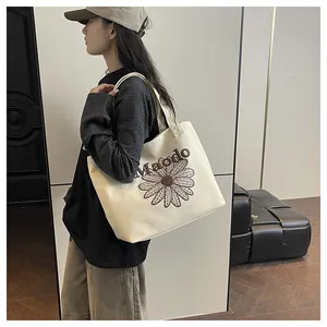 Detail of embroidered daisy flower and Maodo text on a beige canvas tote bag
