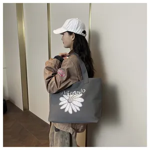 Close-up of gray canvas tote bag featuring white daisy embroidery and Maodo lettering
