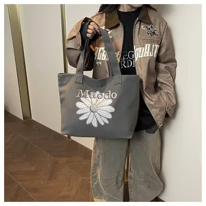 Close-up of grey canvas tote bag featuring embroidered white daisy and Maodo lettering
