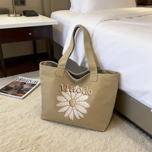 Khaki canvas tote bag with embroidered white daisy and Maodo lettering in home setting