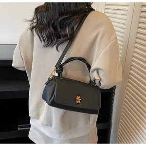 Detail of black pebbled leather crossbody bag with gold metal clasp and ring handle