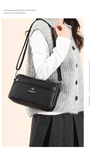 Detalle de bolso bandolera de cuero negro acolchado con logotipo de canguro plateado y cremallera