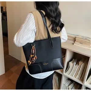 Detail der schwarzen Kontrast-Tote-Bag mit Perlenanhänger und goldener Markenprägung