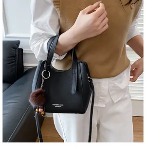 Dettaglio della borsa a secchiello in pelle nera con ciondolo di peluche su modella
