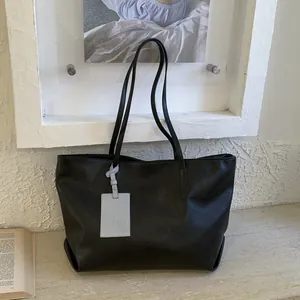 Minimalist large capacity black tote bag made of synthetic leather with a slim shoulder strap