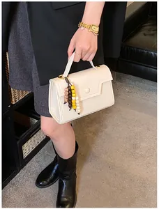 Detail of off-white leather handbag with beaded tassels and round decorative buckle