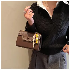 Detail of vintage brown leather handbag with ethnic beaded charm and metal buckle accent