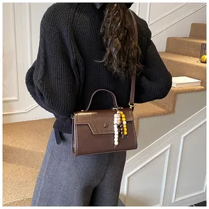 Detail view of a vintage brown leather crossbody bag with beaded charm and top handle