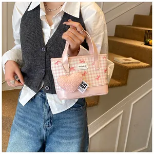 Détail d'un sac seau rose à carreaux avec un nœud rouge et un charme en cœur peluche