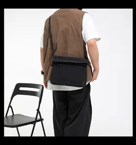 Close-up of black technical canvas messenger bag with adjustable strap on a chair