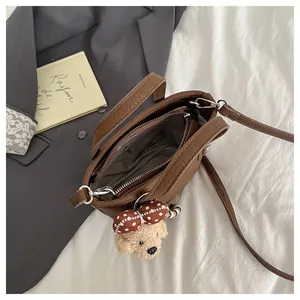 Détail d'un sac seau marron avec breloque ours en peluche et poche intérieure zippée
