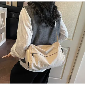 Side view of a large beige crossbody bag with multiple pockets worn by a model