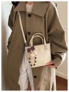 Détail du sac seau en cuir texturé beige avec un adorable pendentif ours en peluche