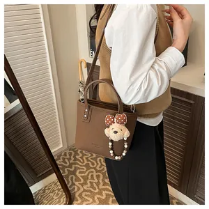 Détail du sac cabas en cuir marron foncé avec breloque ours en peluche et logo gravé