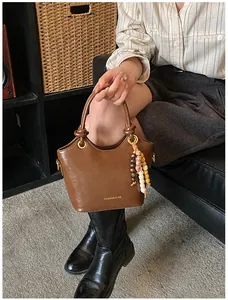 Detalle de bolso tipo cubo de cuero marrón con colgante de cuentas y letras oro