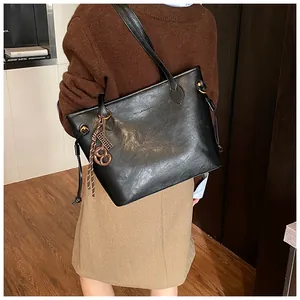 Detail of black faux leather tote bag with round pendant on model's shoulder