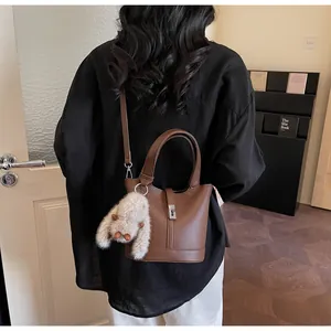 Detail of brown lychee leather bucket bag with silver lock and plush bunny charm