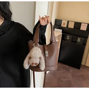 Close-up of brown litchi pattern leather bucket bag with cute plush rabbit charm