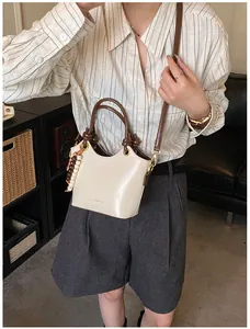 Detalle de bolso crema para mujer con ribete marrón, colgante de cuentas y letras doradas