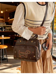 Détail de la broderie de teckel et d'étoiles sur un sac bandoulière en cuir marron poli