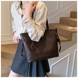 Detail of dark brown tote bag featuring side drawstrings and a round leather charm
