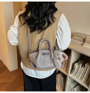 Detailed back view of a light gray pleated crossbody bag with a cute plush rabbit charm