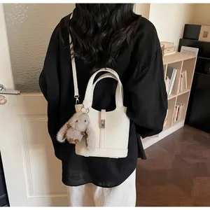 Rear view of cream litchi texture bucket bag with plush bunny charm and shoulder strap