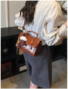 Detail einer braunen Vintage-Satteltasche mit Metallschnalle und Plüschball-Anhänger