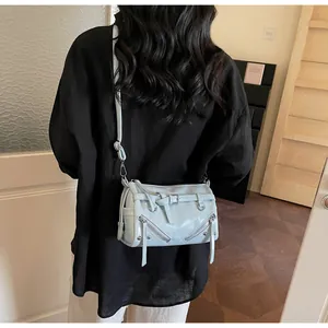 Model wearing a light blue patent leather cylindrical crossbody bag with metal zippers