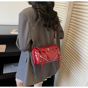 Detail of red glossy leather crossbody bag with metal zippers and long tassel straps