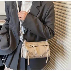 Detail of soft cream leather crossbody bag with decorative belts and silver zippers