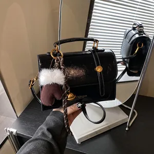 Schicke schwarze Umhängetasche in Glanzoptik mit goldener Hardware und Handschuh-Anhänger