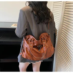 Dettaglio della borsa tote marrone vintage con ciondolo a croce e catena sulla spalla