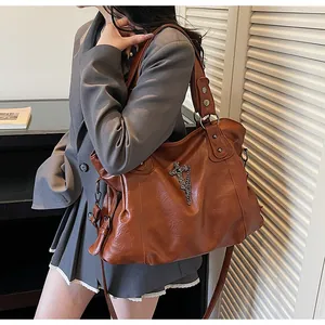 Dettaglio di una borsa tote in pelle marrone con croce d'argento e un blazer grigio