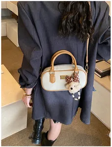 Detail of a beige leather bowling bag with brown handles and a cute bear charm accessory