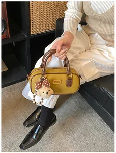 Detail of yellow bowling handbag with brown handles and plush bear charm on a sofa