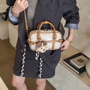 Dettaglio della borsa Boston crema con finiture in pelle marrone e ciondolo a orsetto