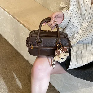 Dettaglio borsa a mano in pelle marrone scuro con finiture oro e ciondolo a orsetto