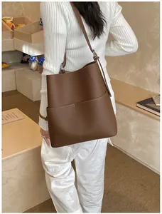 Braune Eimer-Tasche aus strukturiertem Leder am Modell mit minimalistischem Hintergrund