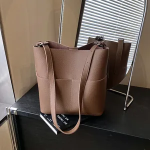 Braune Beuteltasche aus Leder mit Lychee-Muster auf einem schwarzen Schrank mit Spiegelung