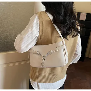 Détail du sac baguette beige en similicuir avec chaîne argentée et pendentif en forme de cœur
